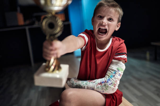 pequeño jugador emocionado sosteniendo el trofeo ganado en el partido. deporte de equipo infantil - physical injury sport child locker room fotografías e imágenes de stock