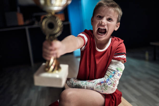 eccitato piccolo giocatore che detiene il trofeo vinto nel match. sport di squadra per bambini - physical injury sport child locker room foto e immagini stock