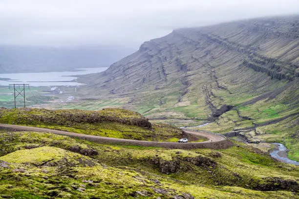 Ring road on route 1 in east Iceland highway with moss green landscape mountains and car on steep slope with overcast cloudy stormy weather in Berufjordur area