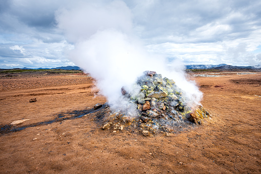 Hot steam rising from pile of rocks geyser in Hverir geothermal spot area in Iceland by Myvatn caldera lake famous place in north Iceland