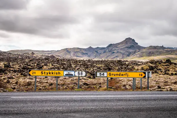 Black lava field on Snaefellsnes peninsula in Iceland with direction signs for Stykkish Stykkisholmur and Grundarfjordur with nobody on empty road