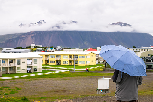 Hofn, Iceland closeup of man holding umbrella back looking at cityscape landscape view of peaceful small fishing village town in rain, raining weather