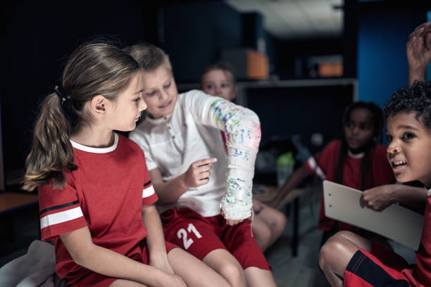 un pequeño jugador mostrando su lesión a un pequeño compañero de equipo. deporte de equipo infantil - physical injury sport child locker room fotografías e imágenes de stock