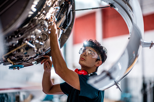 Aircraft mechanic inspecting and checking the technology of a jet engine in the hangar at the airport.