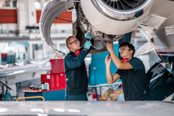 Young aircraft mechanics working on a jet engine in the hangar Two male aircraft maintenance mechanics inspect and check an airplane jet engine in the airport hangar. aerospace industry stock pictures, royalty-free photos & images