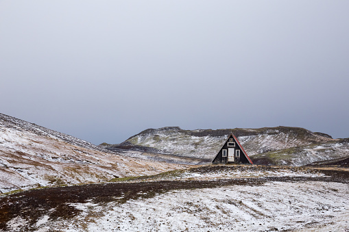 Cabin surrounded by hills covered in the snow under a cloudy sky in Snaefellsnes, Iceland