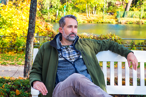 handsome man in his 50s sitting on bench in park in autumn