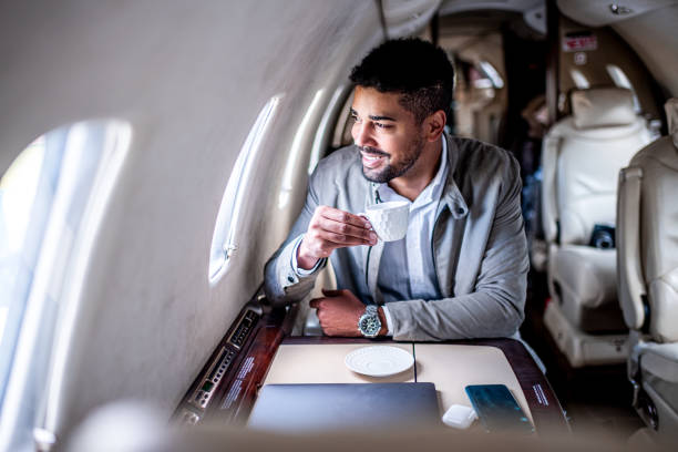 Casual businessman enjoys a cup of coffee during the flight in a corporate plane Young businessman enjoys his cup of coffee after work while sitting in the private jet airplane during the flight on a casual business trip. vehicle interior audio stock pictures, royalty-free photos & images