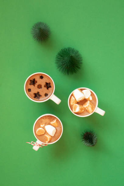 istock White cups with hot cocoa, marshmallows, spice cinnamon decor and Christmas fir tree decor on green background, top view. Winter holidays drinks minimalist flat lay composition 1284119138