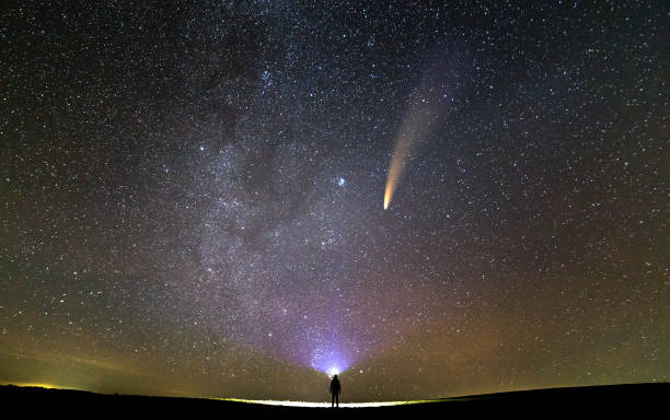 istock Small silhouette of a scientist with flashlight on his head pointing bright beam of light on starry sky with C/2020 F3 (NEOWISE) comet with light tail. Space exploration concept. 1284120896