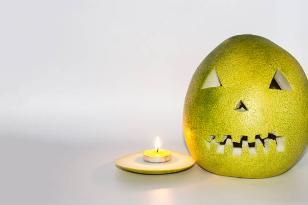Scary face carved in pomelo fruit with candle in front isolated in gray background