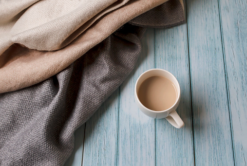 Autumn cozy composition with pastel gray scarf, cup of coffee on blue wooden background with copy space. Autumn morning concept. Banner for website. Flat lay.