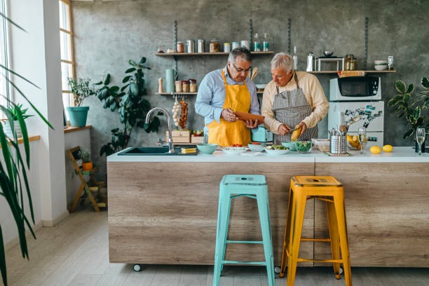 Two men cooking food watching online tutorial using digital tablet Two senior men learning to cook while watching tutorials on internet using digital tablet cooking show stock pictures, royalty-free photos & images