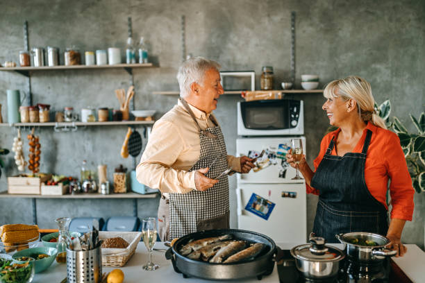 istock Senior couple drinking wine while cooking fish in kitchen 1284122922