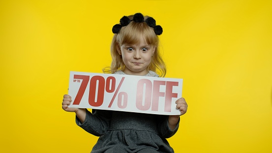Excited child girl showing Up To 70 percent Off inscription, advertising discounts, smiling, looking amazed with low prices, shopping on Black Friday or Cyber Monday. Teen pupil showing thumbs up