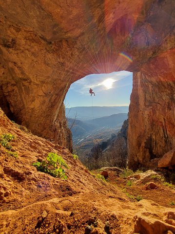 Male rock climber hanging on natural arch