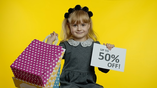 Child girl showing Up To 50 percent Off inscription sign and shopping bags. Teen pupil smiling, looking satisfied with low prices, shopping on Black Friday, Christmas or New Year