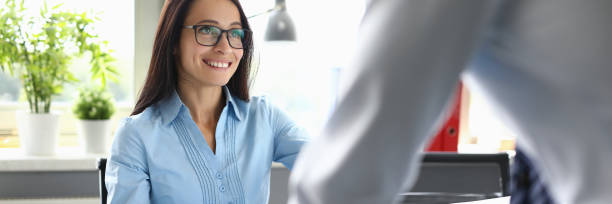 businesswoman with glasses sits in an office at table and communicates with colleague - look for trains” imagens e fotografias de stock