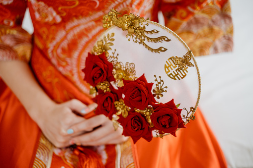 An asian Chinese bride holding a decorative hand fan on wedding day