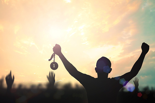 Winner hand raised and holding gold medal reward against sky sunset background