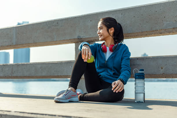 здоровая женщина держит яблочные фрукты и сидит на земле. - water bottle strength foods and drinks smiling стоковые фото и изображения