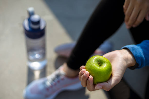 здоровая женщина держит яблочные фрукты и сидит на земле. - water bottle strength foods and drinks smiling стоковые фото и изображения