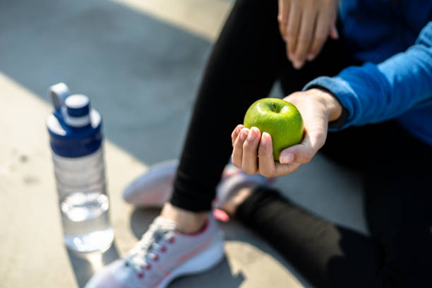 здоровая женщина держит яблочные фрукты и сидит на земле. - water bottle strength foods and drinks smiling стоковые фото и изображения