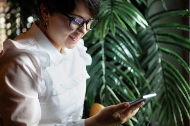 istock Young woman in business white blouse is reading a text message from mobile phone while drinking coffee 1284164458