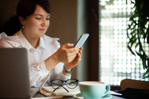istock Young woman in business white blouse is reading a text message from mobile phone while drinking coffee 1284164781
