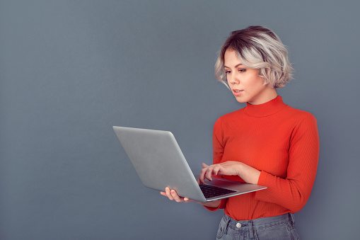Young woman wearing red blouse isolated studio browsing laptop working serious concentrated