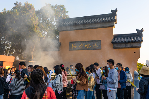 Nanjing, China - October 31, 2020:  Prayers holding incense to pray in ancient Jiming (Rooster Crowing) Temple. Existing temple condtructed in Ming dynasty in late 14th CE, one of oldest ones in City.