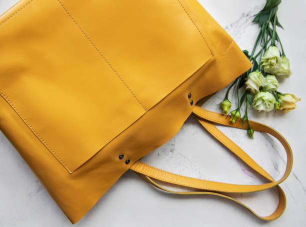 istock Large yellow leather bag and flowers on marble background 1284173572