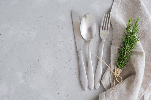 Food cooking background. Serving cutlery on a concrete table. Knife, fork, spoon on a serving napkin with a sprig of rosemary. New Year's table setting.