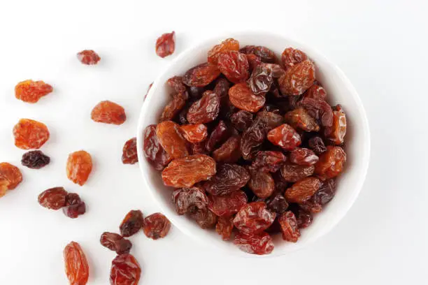 Dried fruit as healthy snack. Bowl with raisins and space for text on white background, top view.
