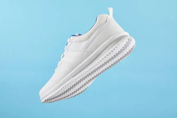 White sports sneakers levitate on a blue background. Stylish man sneakers for fitness.