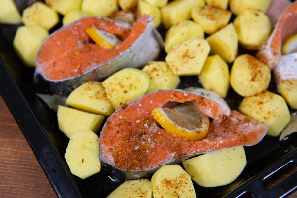 istock Red fish fillet with vegetables and spices on a black baking tray. 1284184883