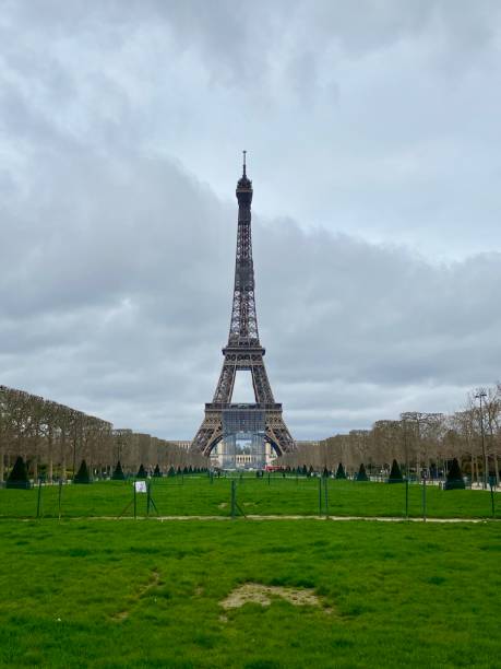 legendary eiffel tower of paris, france standing before dramatic cloudy stormy sky. bright healthy green grass field infront . - eiffel tower paris france france tower imagens e fotografias de stock