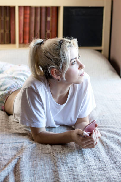 istock Relaxed Blonde young woman lying on bed while holding a mobile phone 1284191915