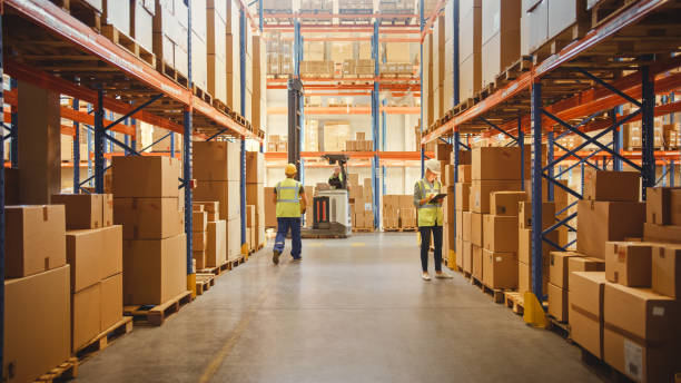 istock Retail Warehouse full of Shelves with Goods in Cardboard Boxes, Workers Scan and Sort Packages, Move Inventory with Pallet Trucks and Forklifts. Product Distribution Logistics Center. 1284193253