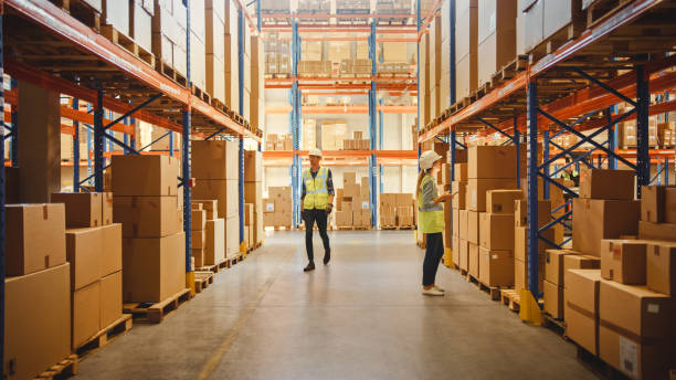 istock Retail Warehouse full of Shelves with Goods in Cardboard Boxes, Workers Walk, Scan and Sort Packages, Move Inventory. Product Distribution Delivery Center. 1284193280