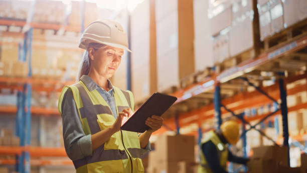 professional female worker wearing hard hat checks stock and inventory with digital tablet computer in the retail warehouse full of shelves with goods. working in logistics, distribution center - cargo container imagens e fotografias de stock