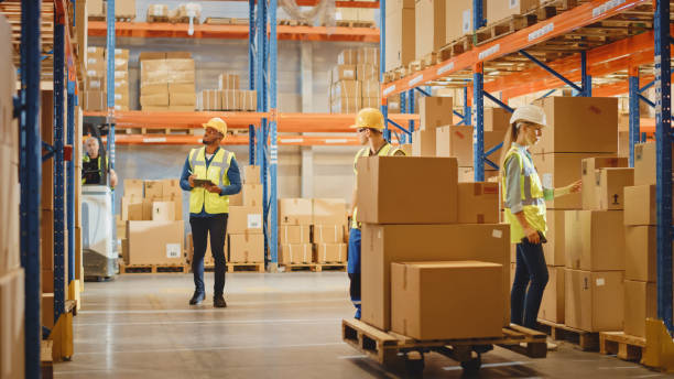 istock Handsome Male Worker Wearing Hard Hat Holding Digital Tablet Computer Walking Through Retail Warehouse full of Shelves with Goods. Professional People Working in Logistics and Distribution Cente 1284193419