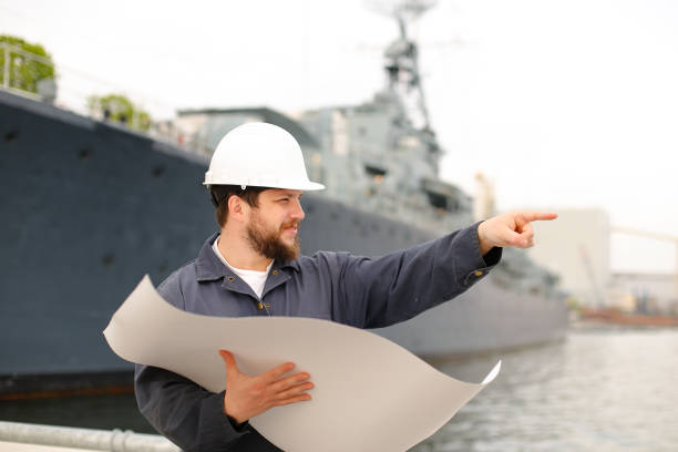 istock Maritime deckhand reading blueprints, showing by forefinger and standing near vessel 1284193508