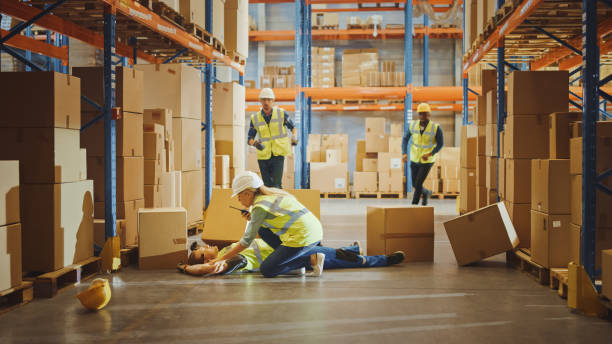 istock Warehouse Worker Has Work Related Accident Falls while Trying to Pick Up Cardboard Box from the Shelf. Colleagues Call for Help and Medical Assistance. Injury at Work. 1284193526