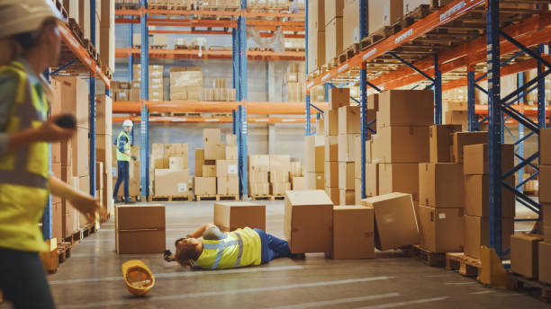 istock Warehouse Worker Has Work Related Accident Falls while Trying to Pick Up Cardboard Box from the Shelf. Colleagues Call for Help and Medical Assistance. Injury at Work. 1284193533
