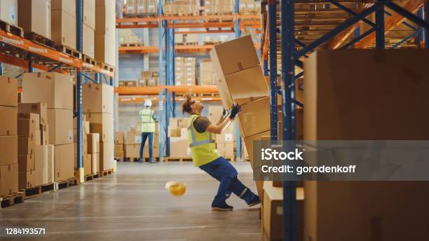 Shot Of A Warehouse Worker Has Work Related Accident He Is Falling Down Beforetrying To Pick Up Heavy Cardboard Box From The Shelf Hard Injury At Work Stock Photo - Download Image Now
