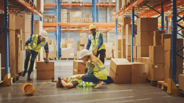 istock Warehouse Worker Has Work Related Accident Falls while Trying to Pick Up Cardboard Box from the Shelf. Colleagues Call for Help and Medical Assistance. Injury at Work. 1284193578