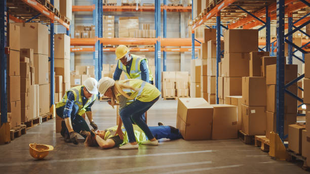 warehouse worker has work related accident falls while trying to pick up cardboard box from the shelf. colleagues call for help and medical assistance. injury at work. - crash imagens e fotografias de stock