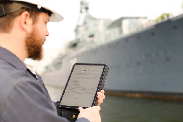 First mate reading contract on tablet near vessel in background