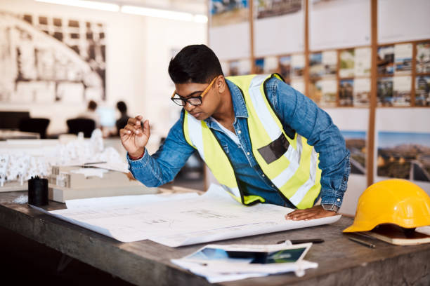 My job is to bring dreams to life Shot of a young architect looking at a blueprint in his office project manager stock pictures, royalty-free photos & images